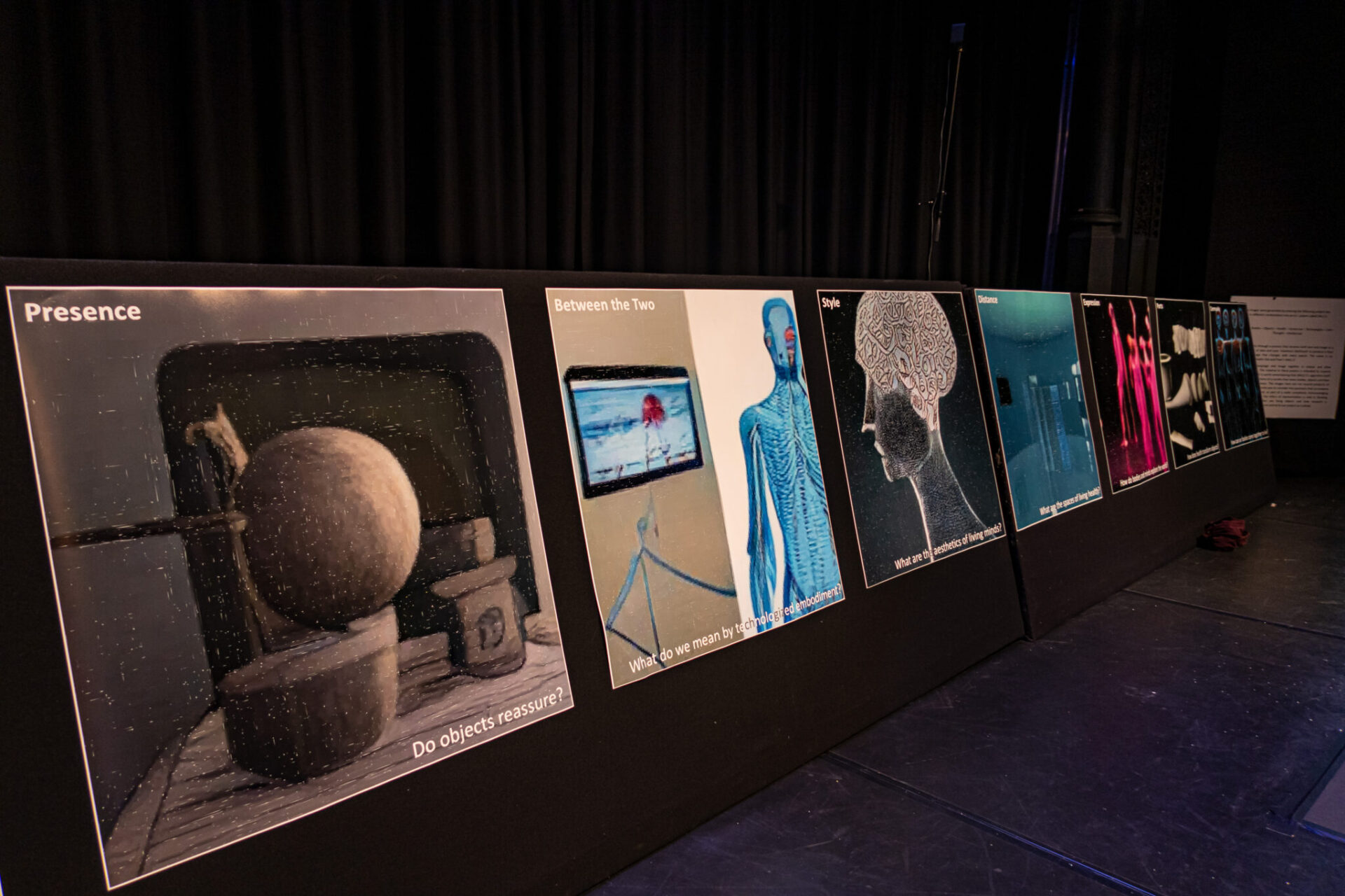 seven A3 prints of AI generated abstract artwork are displayed in a dimly lit workshop as part of an exhibition.