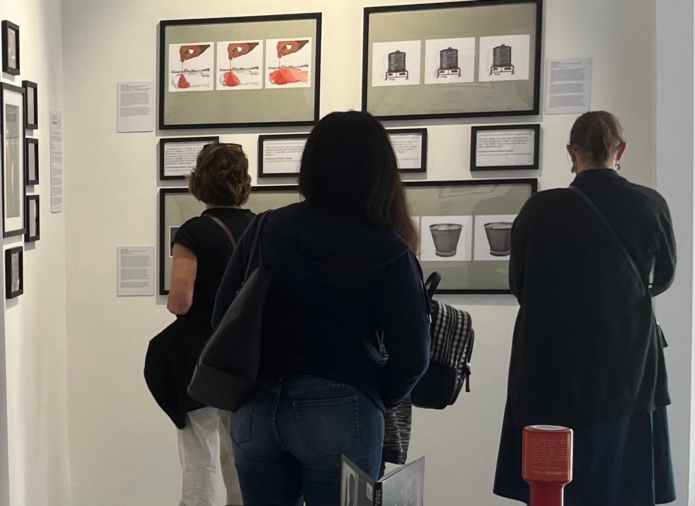 Three exhibition visitors looking at framed artworks and extracts from Bhopal survivors’ stories